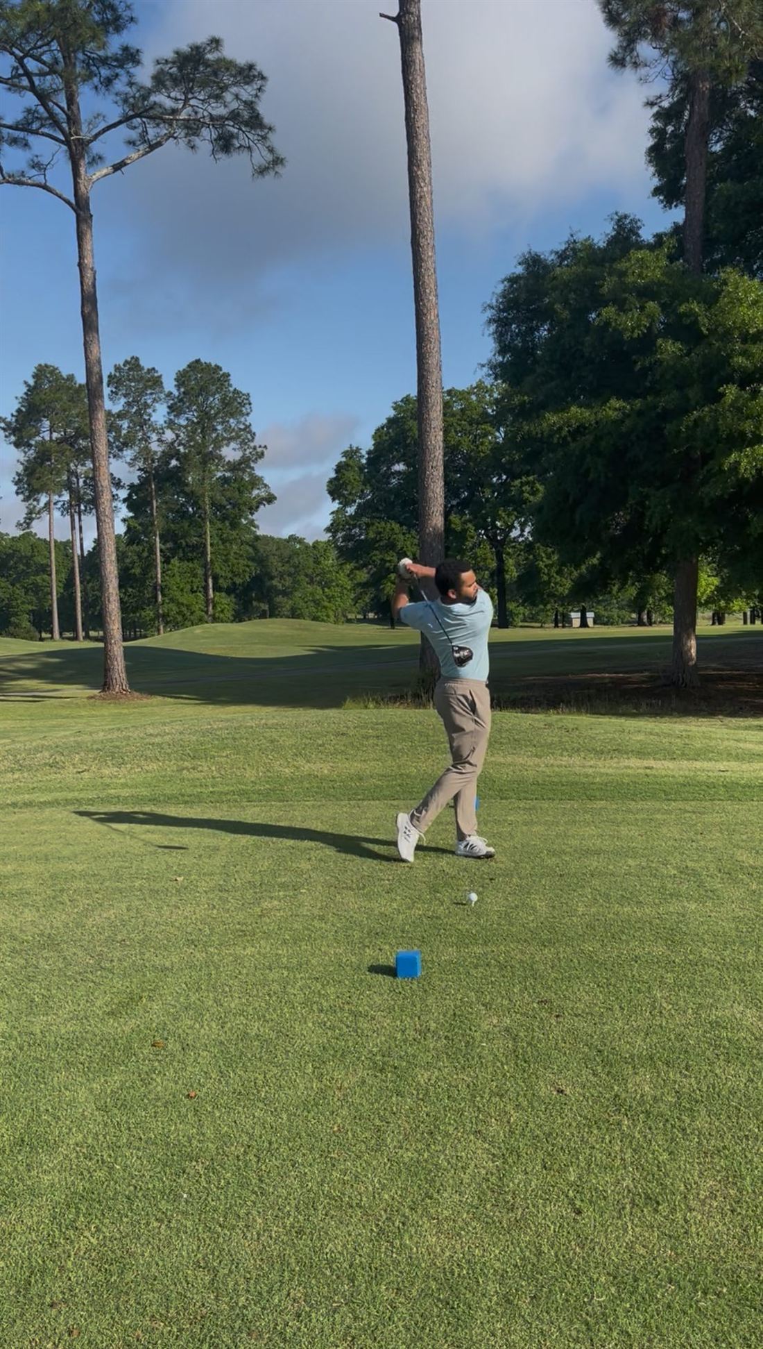Golfer mid-swing on a tree-lined course